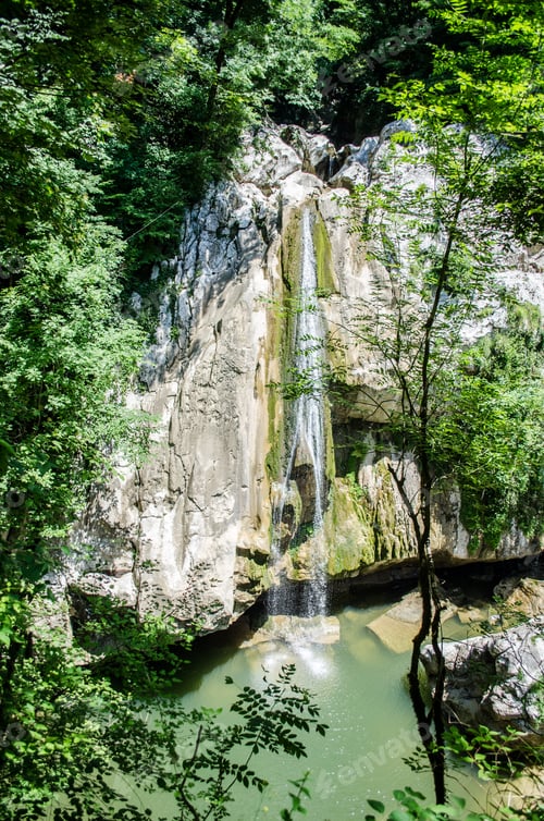 Preview: Tall waterfall cascading over mossy rocks in sunlit gorge