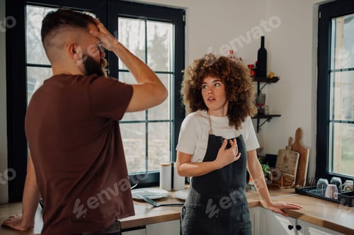 Preview: Young couple arguing in kitchen, woman explaining with hand gestures, man holding head