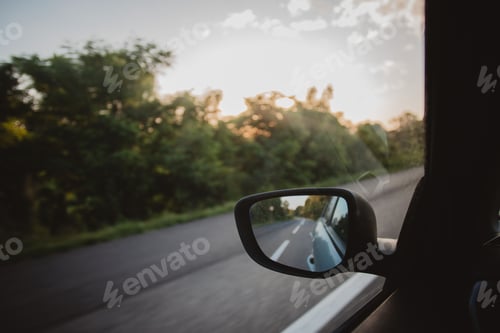 Preview: Closeup of a wing mirror reflecting the car's rear side while driving.