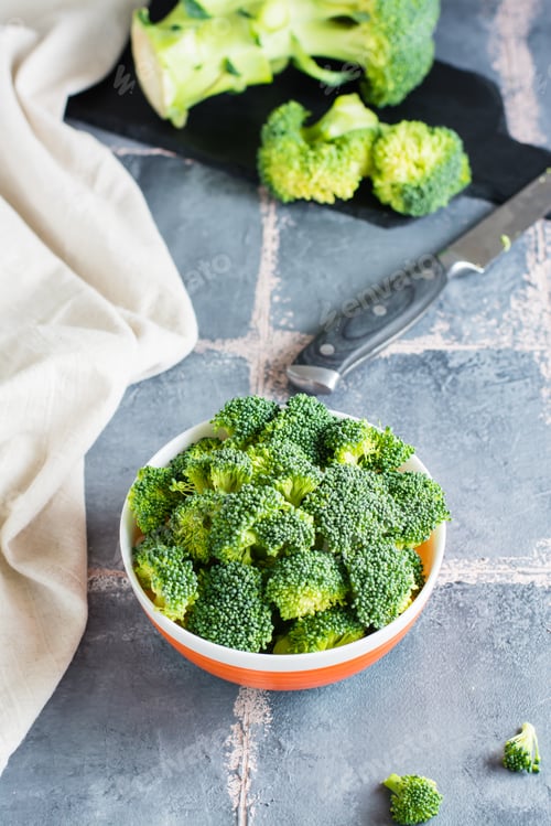 Preview: Pieces of raw broccoli in a bowl and a knife on the table. Cooking healthy vegetarian food.