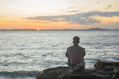 Preview: View of a man sitting in front of the sea enjoying the sunset