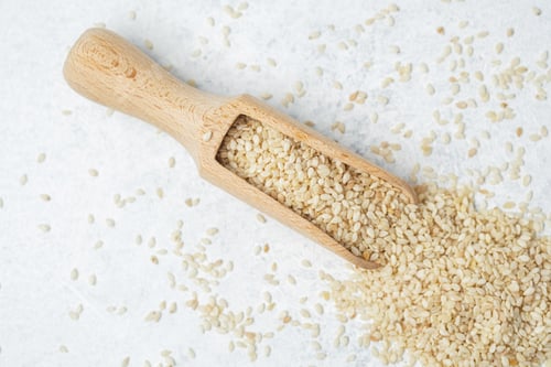 Preview: Scoop filled with sesame seeds on a light surface with scattered seeds