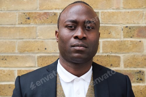 Preview: Serious Businessman Locks Eyes with the Camera Against a Brick Wall