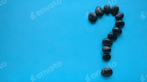 Preview: Top view of question mark symbol by black stone on blue background with copy space.