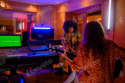 Preview: Latino woman sitting on soundboard while working in a music studio