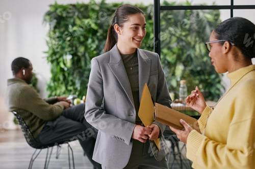 Preview: Young Caucasian Woman Discussing Business Documents with Black Woman Colleague