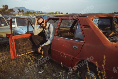 Preview: Bearded Adult Leaning out of Car at Junkyard