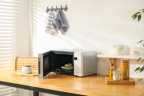 Preview: Open microwave oven with piece of lasagna and kitchen utensils on wooden table indoors