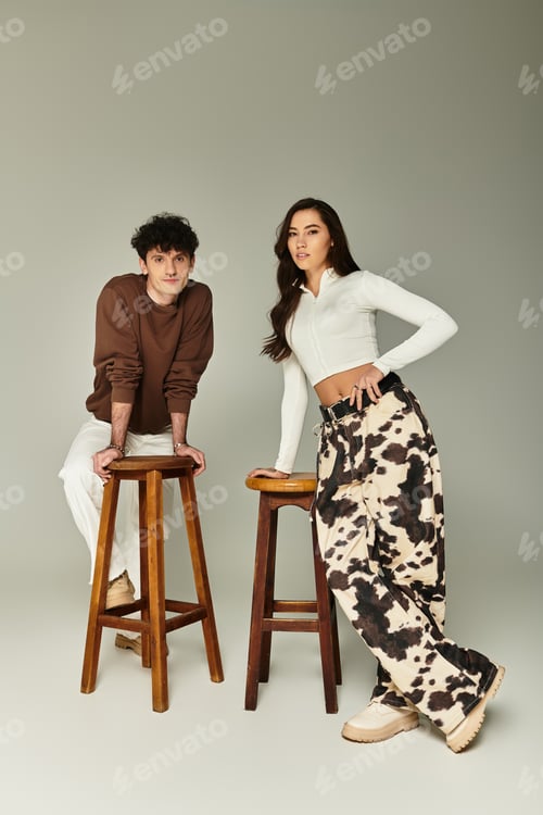 Preview: Stylish young adults posing confidently on wooden stools in a minimalist studio setting
