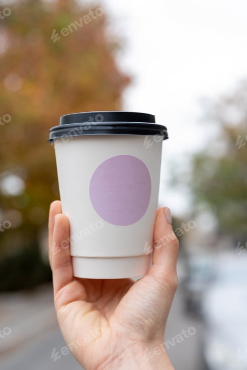 Preview: Young female hand holds paper cup of coffee, take away. Tree background