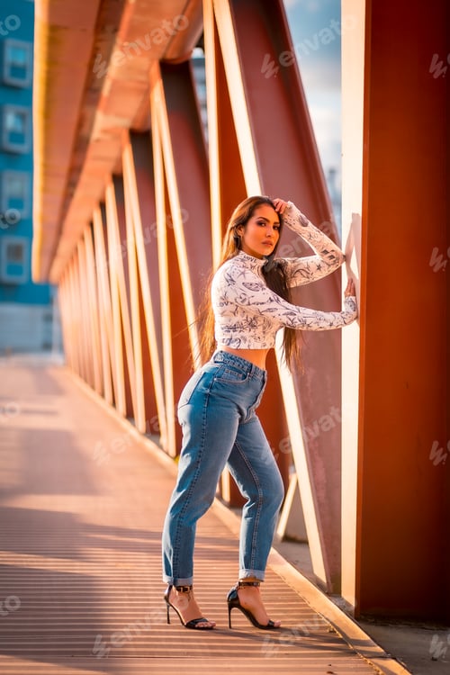 Preview: A brunette Latin girl in a jeans in the city at sunset in an orange jumper