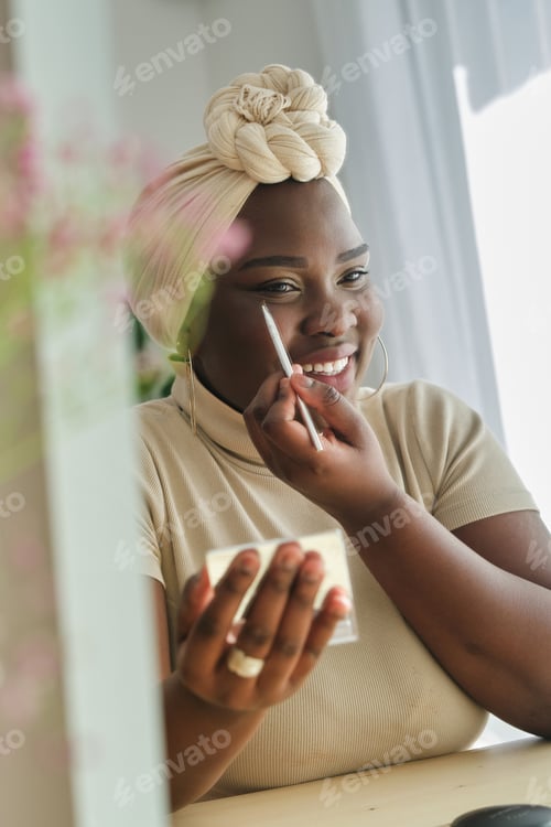 Preview: Cheerful African American lady looking in mirror and applying ma