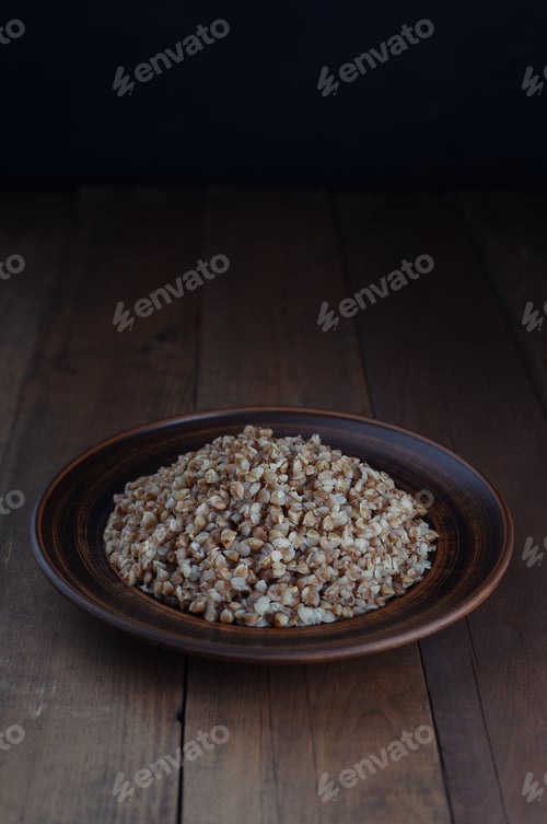 Preview: Boiled buckwheat porridge in a clay plate on a wooden background.