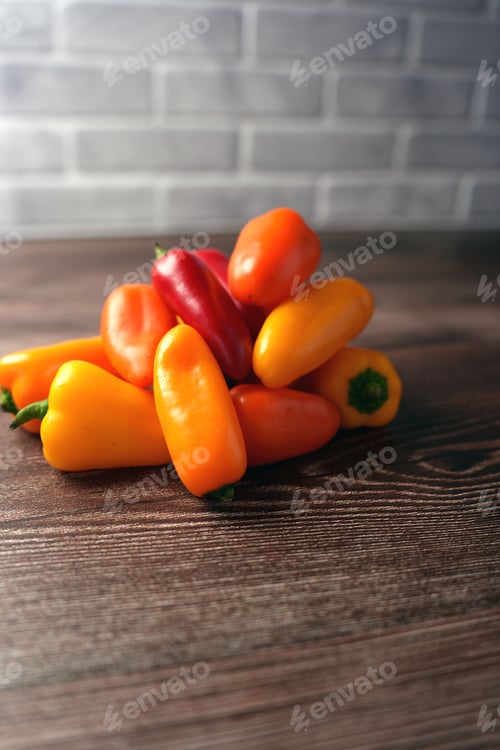 Preview: Bell peppers on wooden surface against gray brick wall show freshness and texture in rustic setting.