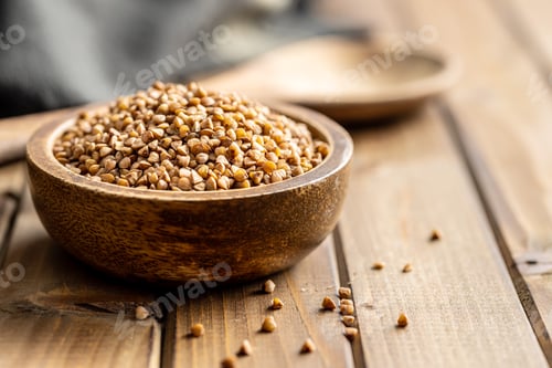 Preview: Uncooked buckwheat grain in bowl on wooden table.