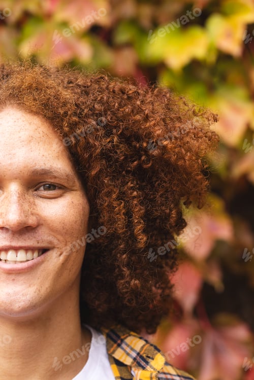 Preview: Half portrait of happy biracial man with red curly hair and freckles smiling in autumn garden