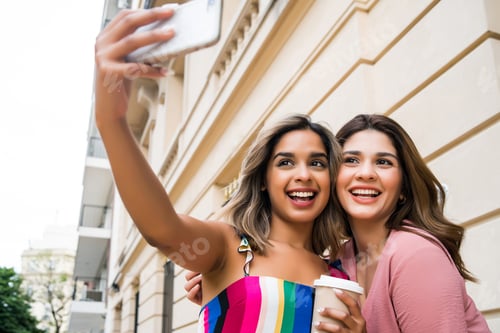 Preview: Two friends taking selfie with phone outdoors.