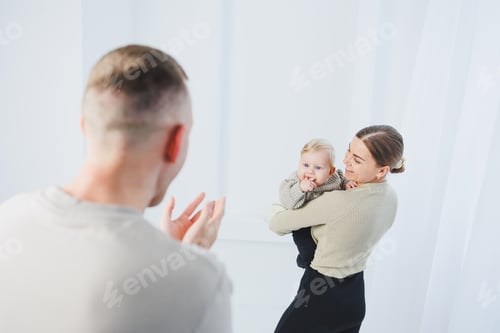 Preview: Young parents mom and dad are playing with a baby on a white background. A married couple hugs