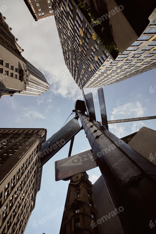 Preview: bottom view of street pole with traffic signs near tall buildings against blue sky in new york city