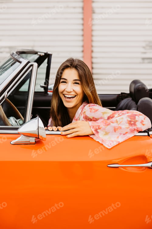 Preview: Young woman laughing and enjoying road trip in orange convertible car