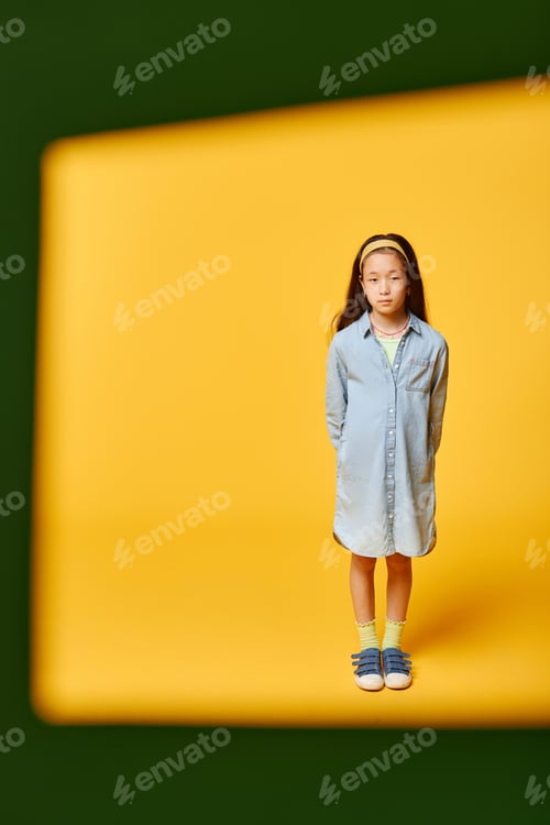 Preview: Confident Preteen Girl in Shirt Dress Standing in Yellow Background in Studio