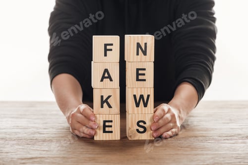 Preview: cropped image of journalist holding wooden cubes with words fake news at wooden table