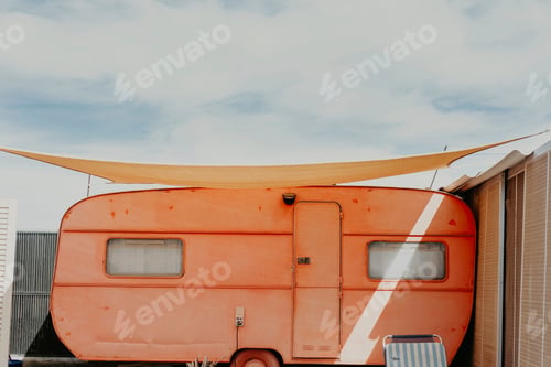 Preview: Vintage orange caravan under a blue sky with shade canopy