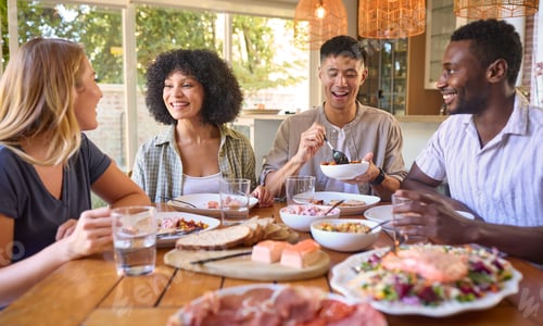 Preview: Group Of Multi-Racial Friends Sitting Around Table Enjoying Meal At Home Together