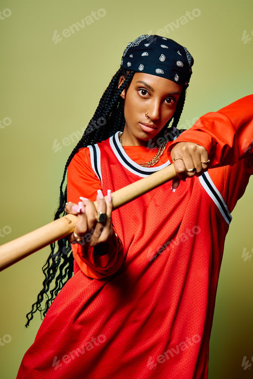 Preview: A young woman presents strength and style, holding a bat with an intense gaze in a studio setting.