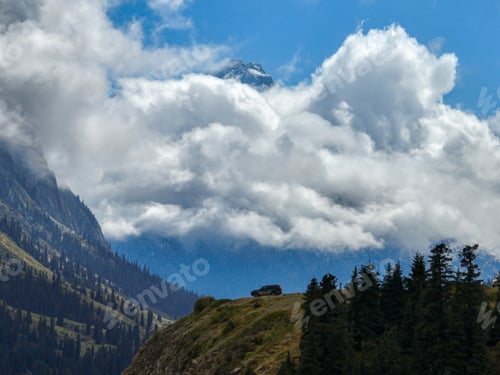 Preview: Off-road vehicle on a mountain slope with obscured snowy peaks