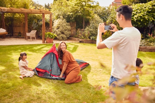 Preview: Asian Father Taking Photo On Mobile Phone As Put Up Tent Family In Garden At Home