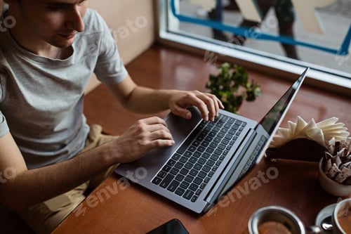 Preview: Millennial student using laptop at cafe. Young man using technology and holding hands on keyboard