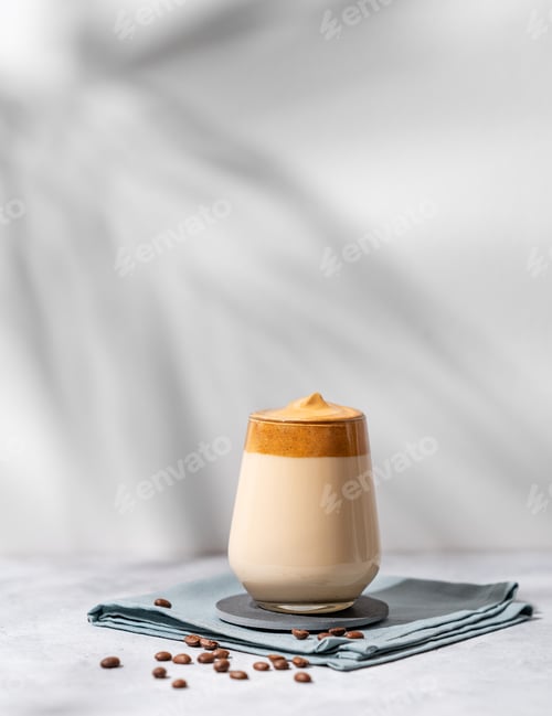 Preview: Dalgona coffee. Whipped instant coffee in a glass with beans and shadow on a light background.