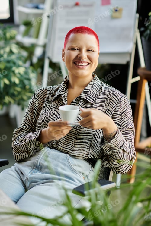 Preview: Brightly smiling bald woman enjoying coffee in a trendy workspace filled with greenery