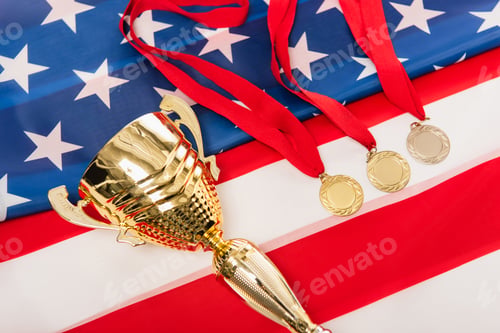 Preview: high angle view of golden medals and cup on american flag