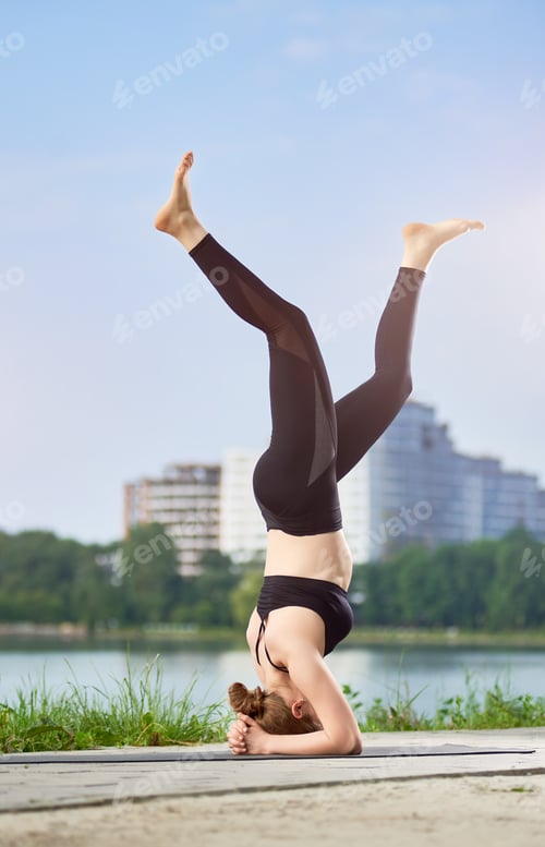 Preview: Yoga girl doing asana Shirshasana, standing on her head outdoor. Morning training for energy boost