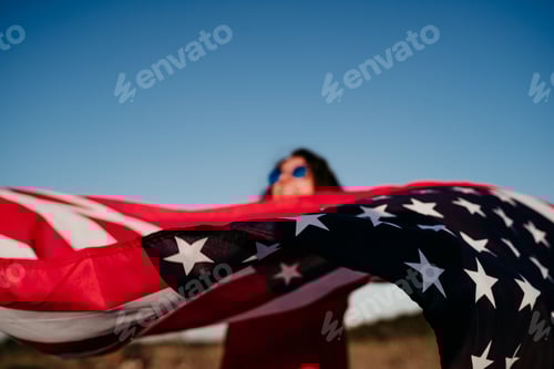 Preview: young woman holding a United States Flag over blue sky. 4th July in America concept