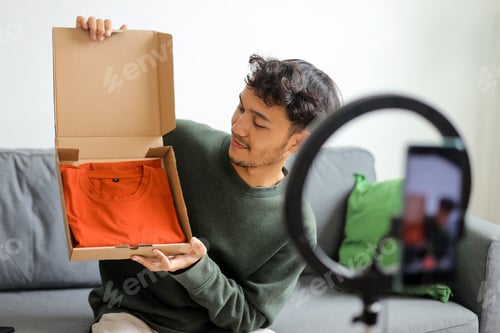 Preview: Young Influencer Unboxing Orange T-Shirt Showcasing The Product During Live Stream
