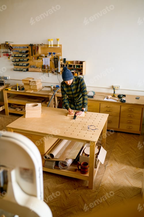 Preview: Man carpenter making technical drawing with pencil on wooden board