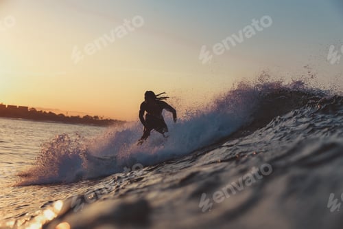 Preview: Man on surf board on waving water at sunset