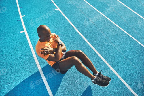 Preview: Fit and focused young athlete doing crunches on a track