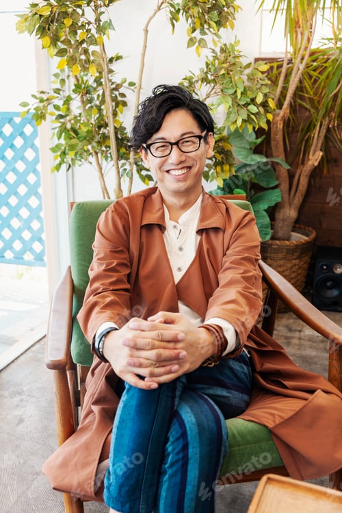 Preview: Male Japanese professional sitting in a co-working space, smiling at camera.