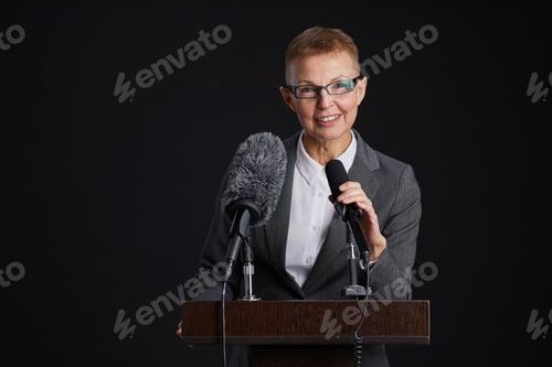 Preview: Mature Woman Speaking to Microphone at Podium