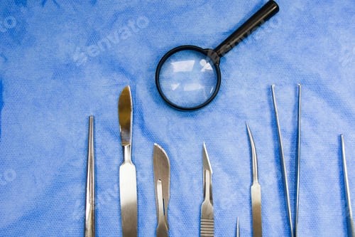 Preview: Closeup of a stainless dissection kit near a magnifier on a blue surface