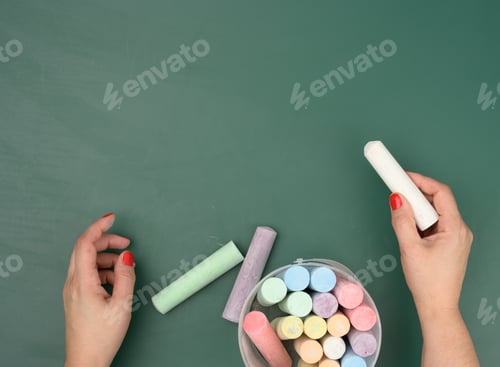 Preview: Hand holds a piece of white chalk on the background of an empty green chalk board