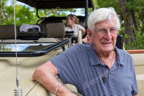 Preview: A senior man standing by a safari jeep smiling.