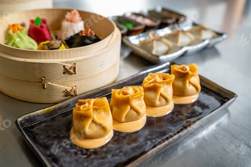 Preview: Colorful dumplings on black plate with bamboo steamer in background