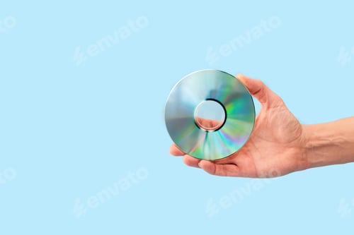 Preview: Close up of Hand holding compact disc on light blue background