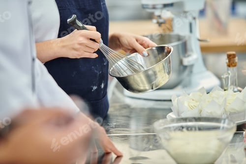 Preview: cropped view of young woman with apron whisking ingredients next to chief cook, confectionery