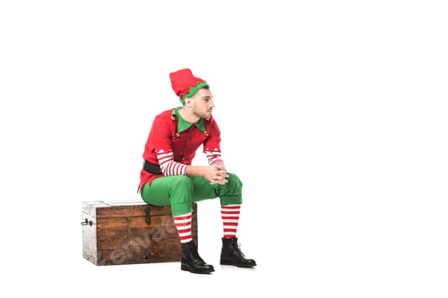Preview: pensive man in christmas elf costume sitting on wooden chest isolated on white